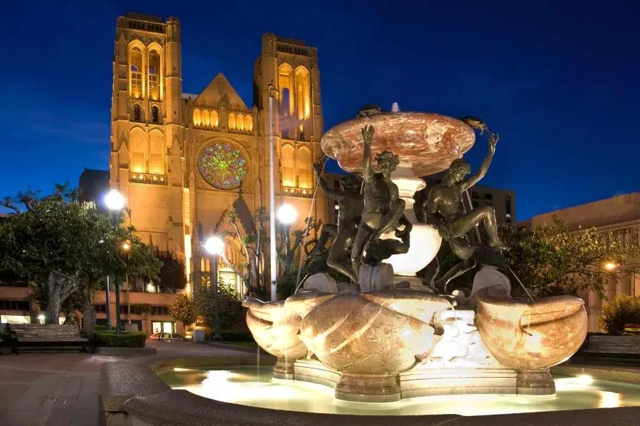 A Grace Cathedral de São Francisco é retratada à noite 和 uma fonte de água ornamentada em primeiro plano.