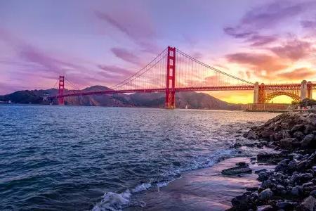 El 金门大桥 al atardecer con un cielo multicolor y la Bahía de San Francisco en primer plano.